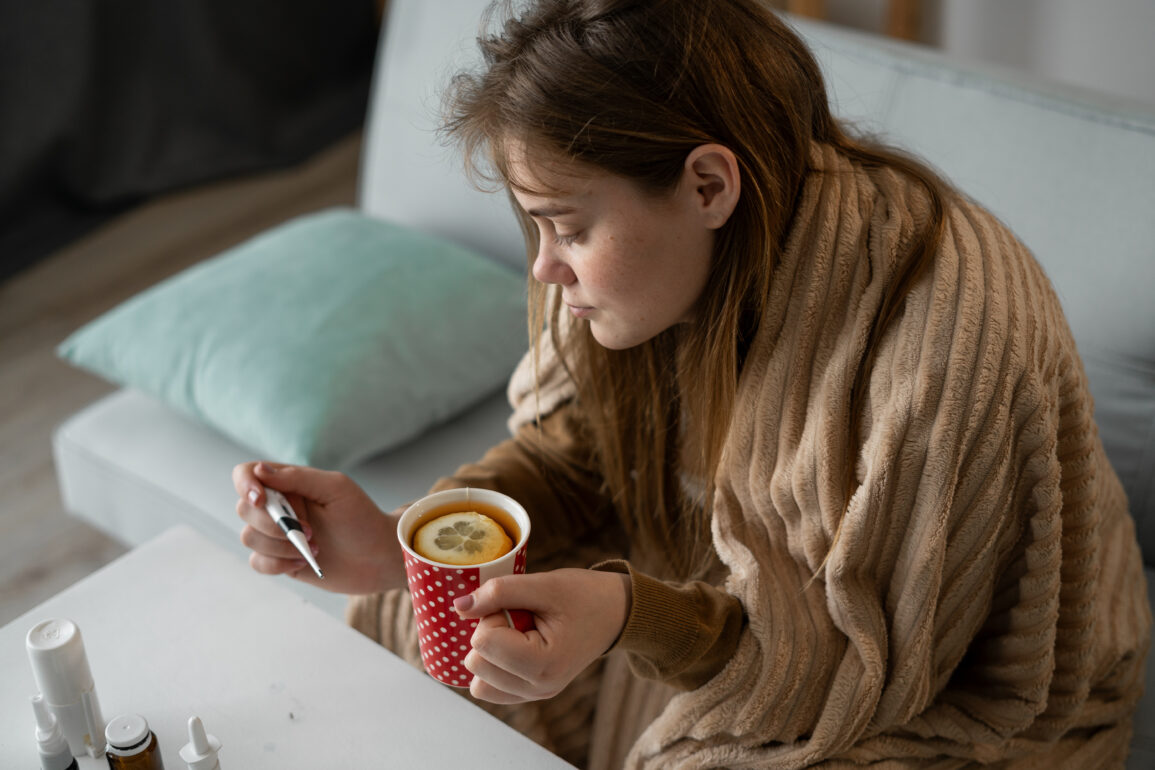 sick woman takes her temperature and drinks tea with lemon for cold. viral infection. Copy space